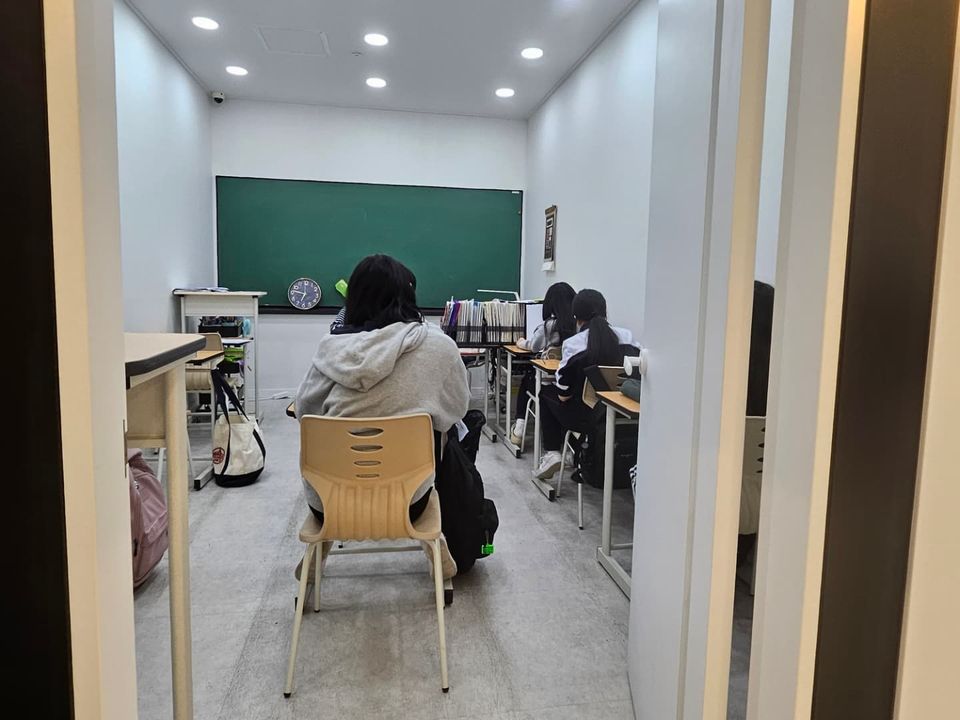열린 문틈으로 본 교실. 학생들이 칠판 앞에서 공부하고 있습니다